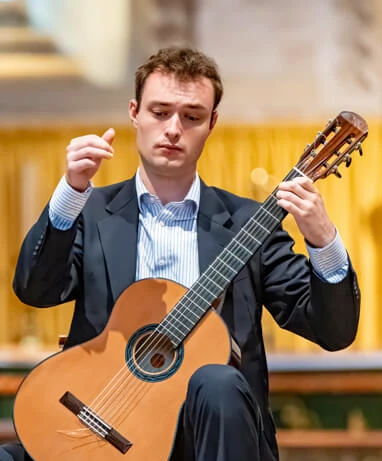 Declan Hickey holding a classical guitar for Fogel Academy testimonial